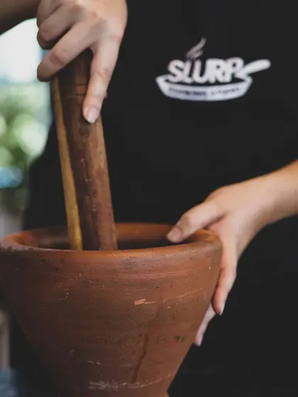 A student learns to use a traditional mortar and pestle, connecting with the timeless methods of flavor extraction.