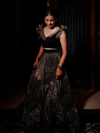 A full-length portrait of a bride in a stunning black and gold lehenga. We use dramatic lighting to showcase the intricate details and sparkle of the outfit.