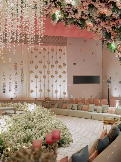 A seating area with a backdrop of hanging Sanskrit verses, creating a sacred and meaningful atmosphere for the wedding ceremony. The floor is covered in a sea of white flowers.