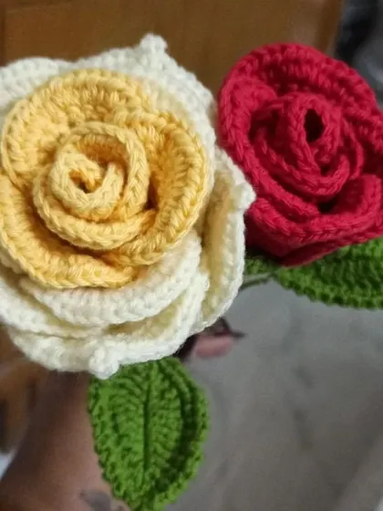 A pair of my handmade crochet roses, showing the color variety I offer. One is a classic red, and the other is a two-tone design with a yellow center and white petals.