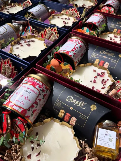 A premium Diwali hamper curated for Aum Papers. This box features artisanal tea, gourmet chocolates, and a hand-poured candle with rose petals, all in a rich, festive color palette.