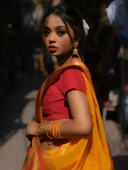 A beautiful three-quarter profile shot in a traditional saree. The makeup is highlighted by a bold red lip and defined eyes, with hair elegantly styled with a flower.