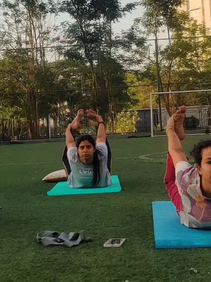 Students in an outdoor class practicing Dhanurasana (Bow Pose). This is a powerful backbend that strengthens the back muscles and opens up the chest and shoulders.