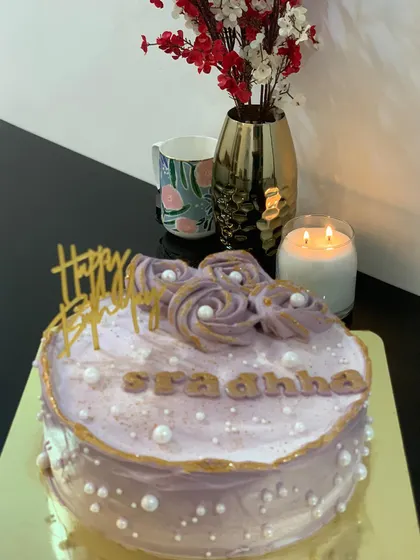 A lovely lavender-colored cake with piped roses and gold accents. The delicate pearl sprinkles add a touch of elegance.
