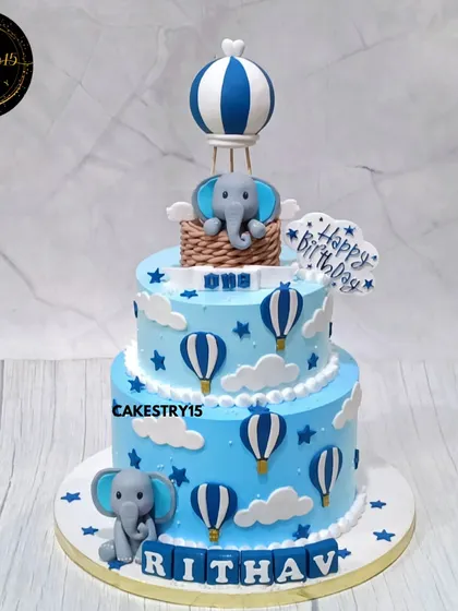 A charming two-tier elephant and hot air balloon cake. This 3kg choco-vanilla cake is decorated in shades of blue with fondant clouds, stars, and a cute elephant topper.