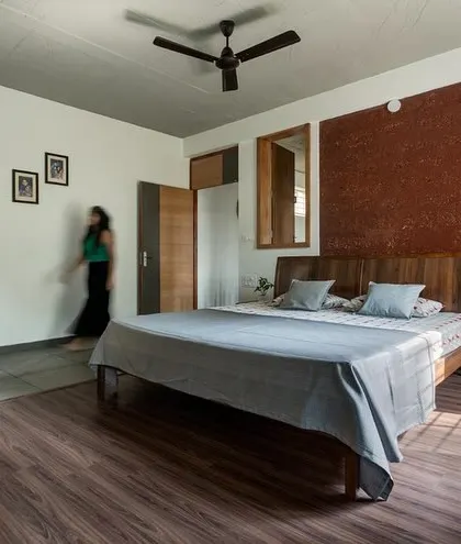 A wider view of the bedroom, showing how natural light fills the space. The combination of rustic textures like the laterite panel and smooth finishes creates a balanced, contemporary feel.