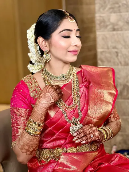 This bride's look is all about traditional elegance. The makeup features golden eyeshadow and a defined lip, complementing her layered gold necklaces and bright pink Kanjivaram saree.
