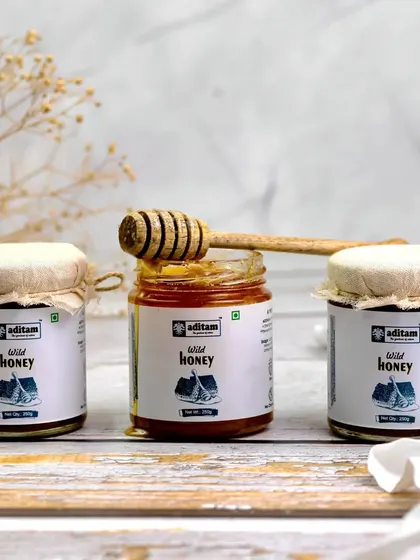 Three jars of wild honey are lined up in a clean, minimalist composition. A honey dipper rests on the open center jar, creating a simple yet inviting image that focuses on the product's natural appeal.