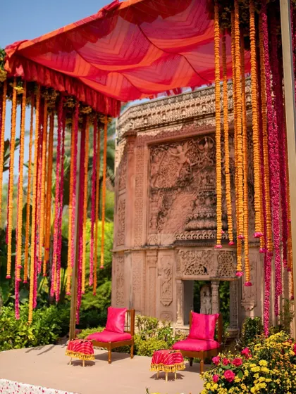 The vibrant Mehendi seating at an ancestral home, with a backdrop of ancient carved stone. The bright pink chairs and hanging marigold strings created a beautiful contrast with the historic setting.