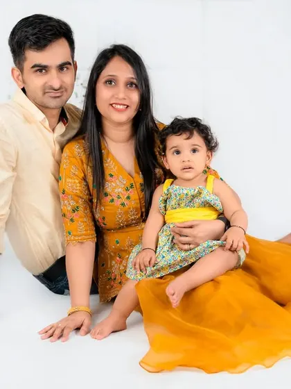 A complete family portrait with everyone dressed in warm, sunny colors. The parents and their baby girl look happy and relaxed together.