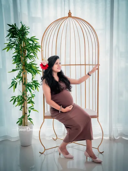 A whimsical and charming studio portrait. The mom-to-be sits in a lovely birdcage-style chair, creating a unique and sweet maternity photo.
