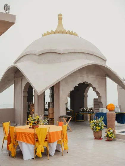 An outdoor seating arrangement under a traditional dome-shaped structure, decorated with bright orange and yellow tablecloths for a festive meal.