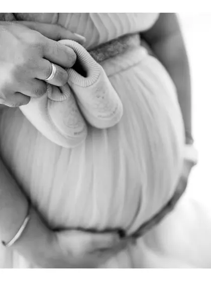 A close-up black and white shot of a couple's hands holding baby shoes against the bump. This detailed shot is full of emotion and anticipation.