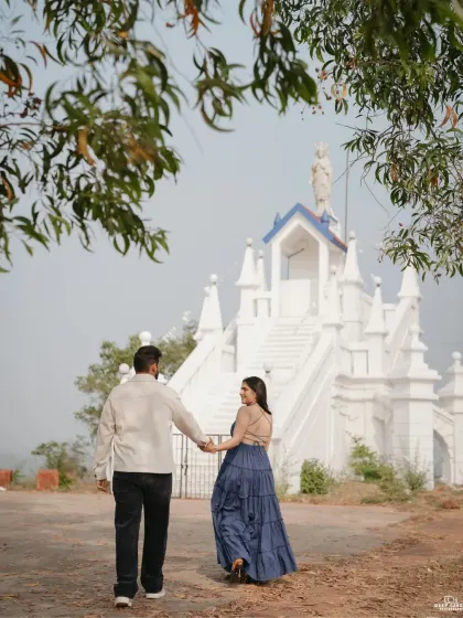 A candid shot of the couple walking away from the church hand-in-hand, framed by lush green foliage, creating a natural and romantic scene.
