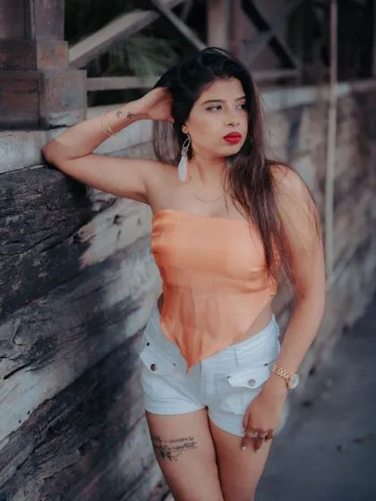 A portrait of a model in a casual outfit against a wooden wall. The texture of the background and her relaxed pose create a warm and stylish image.