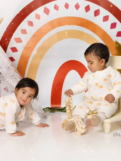 Twin babies exploring our boho rainbow setup together, one crawling while the other sits sweetly on a chair.
