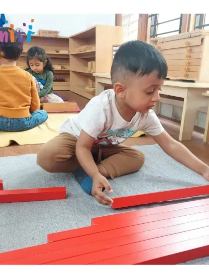 A child arranges the red rods, a classic Montessori sensorial material, from shortest to longest. This activity provides a concrete introduction to the concept of length and dimension.