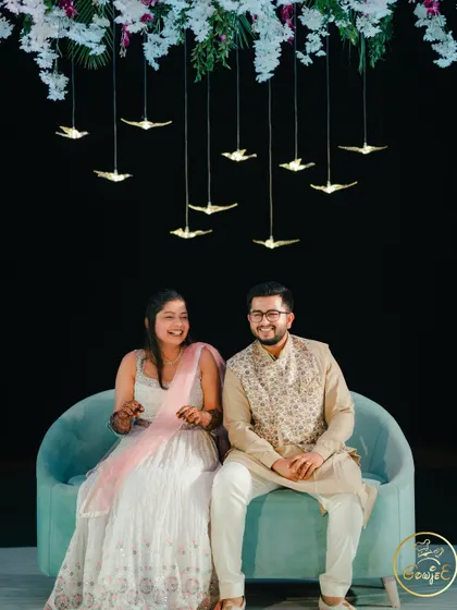 The couple sharing a laugh on a modern turquoise sofa, with artistic bird-shaped lights hanging above.