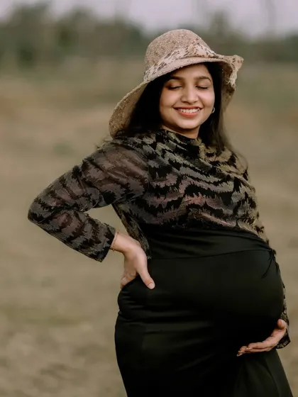 A solo maternity portrait capturing the pure happiness of a mother-to-be. Her joyful smile and the natural, open field setting create a sense of peace and contentment. The simple hat adds a touch of timeless style.