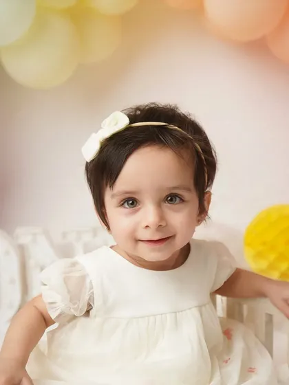 A sweet, gentle smile from the one-year-old. Her delicate dress and the soft lighting make this a truly angelic milestone portrait.