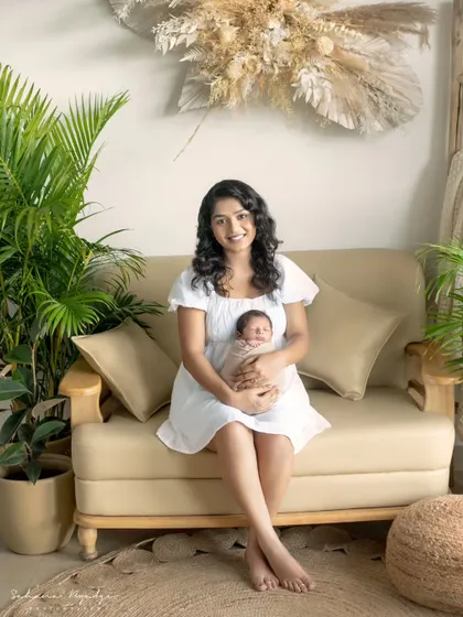 A mother sits with her newborn on a comfortable sofa in my studio. The natural light and green plants create a serene and homely feel for this mother and baby portrait.