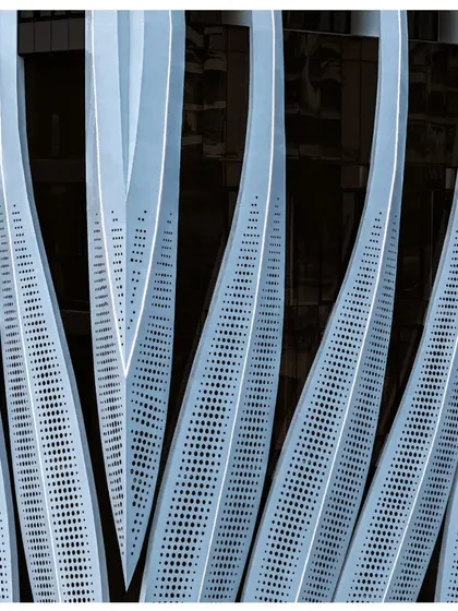 A detailed view of the perforated calligraphic facade of the ID Origins tower. This element is not just aesthetic; it is a performance-driven screen designed to reduce solar glare for the commercial floors while maintaining a lightweight, elegant appearance.