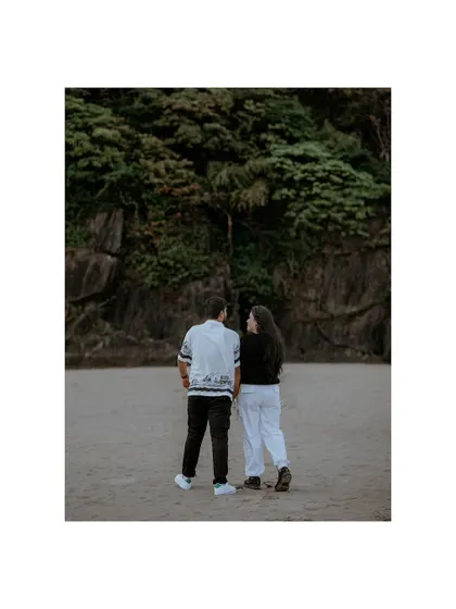 A beautifully framed shot of the couple from behind, their figures small against the vastness of the beach and cliffs.