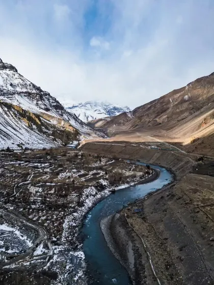 A drone shot capturing the winding Spiti River with snow-capped mountains in the background.