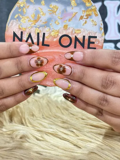 This sophisticated design combines earthy brown tones with delicate floral art. We used a sheer nude base and added gold chrome outlines and tiny rhinestones for a touch of elegance, making it perfect for festive occasions like Rakhi or Teej.