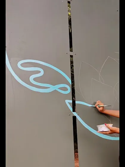 The beginning stages of a new mural. Here, you can see my hand sketching out the initial design and painting the first light blue outlines on a large grey panel.
