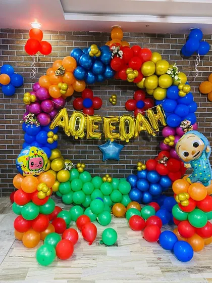 Another angle of the colorful Cocomelon birthday setup. This view shows the full balloon ring and character balloons against a brick-textured wall.