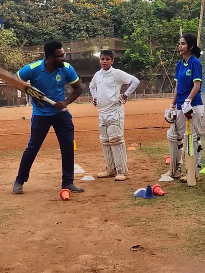A coach demonstrates the correct batting swing to two young players, one boy and one girl. This highlights our inclusive approach and the detailed instruction we provide to all our athletes.