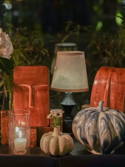 Eclectic decor elements, including terracotta face sculptures and patterned pumpkins, are mixed with small floral accents. This demonstrates our ability to curate unique objects to build a specific mood.