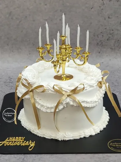 A vintage coquette bow cake with a classic candelabra topper. The white frills and golden ribbons create a look of timeless elegance for an anniversary.
