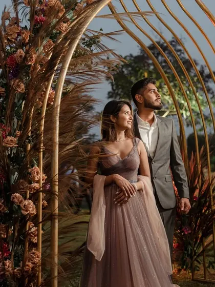 A beautiful couple portrait from an engagement shoot. The golden arches adorned with pampas grass and dried florals create a warm, rustic, and romantic setting.