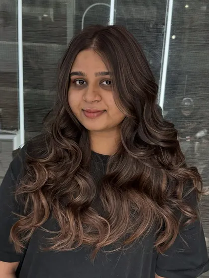 A client showcasing her new chestnut brown hair color. This shade is a beautiful, warm brown with subtle lighter tones, styled into classic waves for a timeless look.