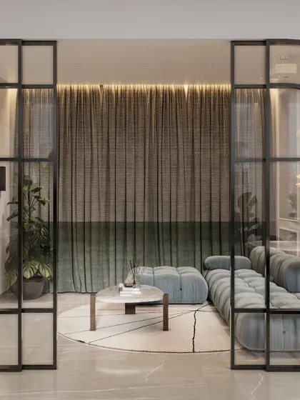 A view into a serene sitting area through modern, black-framed glass doors. The soft blue sofa and layered velvet curtains create a cozy and sophisticated ambiance, perfect for quiet reflection.