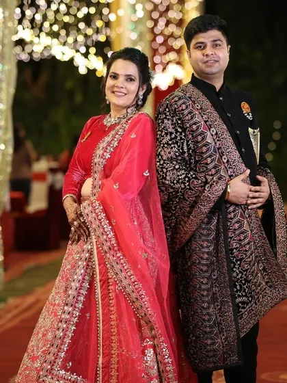 Here is a beautiful example of a coordinated reception look. The bride is wearing a stunning red velvet and net lehenga, while the groom complements her in a classic black sherwani paired with a detailed shawl.