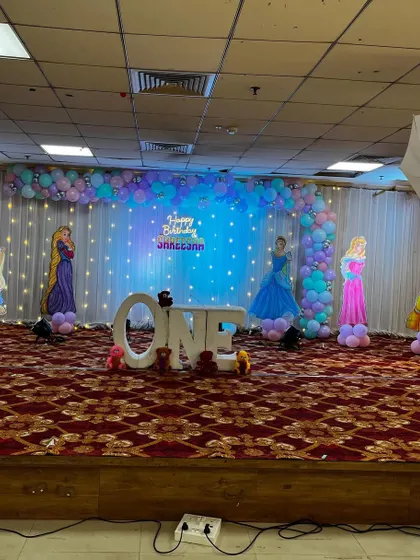 A beautiful princess-themed stage for a first birthday. The decor features an L-shaped balloon arch against a backdrop of fairy lights, creating a dreamy effect.