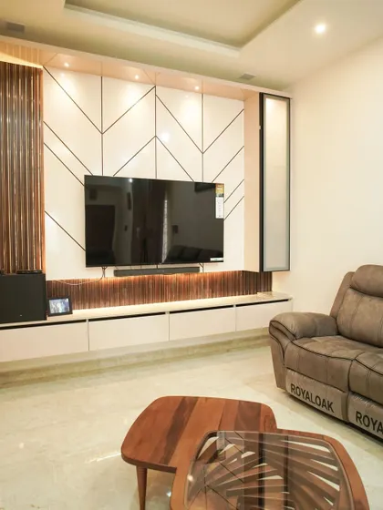 A modern and sleek TV unit with a white console and a back panel featuring a geometric chevron pattern and dark wood fluting. The design is clean, contemporary, and visually dynamic.