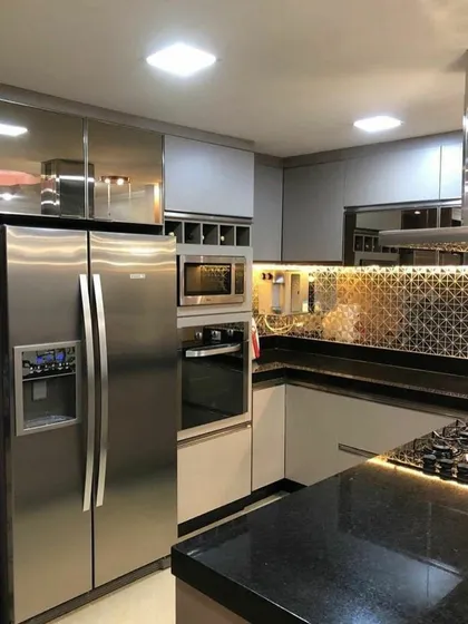 A compact and luxurious kitchen design. This space features reflective high-gloss cabinets, a patterned tile backsplash, and integrated stainless steel appliances, maximizing both style and efficiency in a smaller footprint.