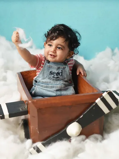 Another little pilot in the clouds, this time playing with the soft cotton. The denim overalls and striped shirt add a classic, boyish charm.