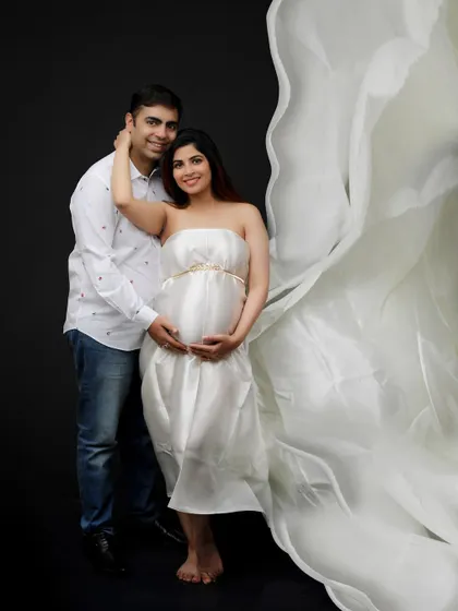 For a touch of modern romance, I love using flowing fabrics and dramatic lighting. This maternity portrait captures the expecting mother in a beautiful white gown, creating an ethereal and goddess-like image against a simple dark background.