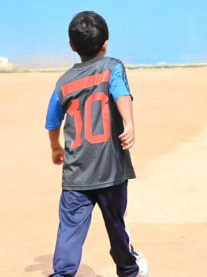 A young player walking onto the field, ready for the game. We focus on building not just skills but also the right attitude and body language for a cricketer.