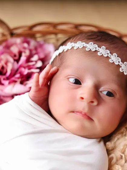 A close-up portrait of a newborn in a white swaddle, looking thoughtfully to the side. This captures a quiet, contemplative moment.