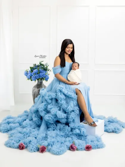 A mother's love personified. She sits elegantly in a cascading blue gown, cradling her newborn baby in a serene and classic portrait.