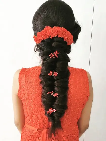 A classic puff hairstyle with a long, thick braid. The look is completed with red floral accessories for a traditional and vibrant finish.