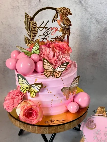 A pretty pink ombré cake decorated with pink chocolate spheres, fresh carnations, and delicate wafer paper butterflies.