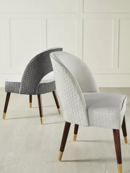 A pair of modern dining chairs with textured upholstery and tapered legs. The composition highlights the elegant, curved back and sophisticated design.