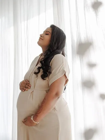 This serene portrait captures the peaceful joy of pregnancy. Her makeup is minimal, with soft contouring and a neutral lip, paired with loose curls to create an effortless and beautiful look.